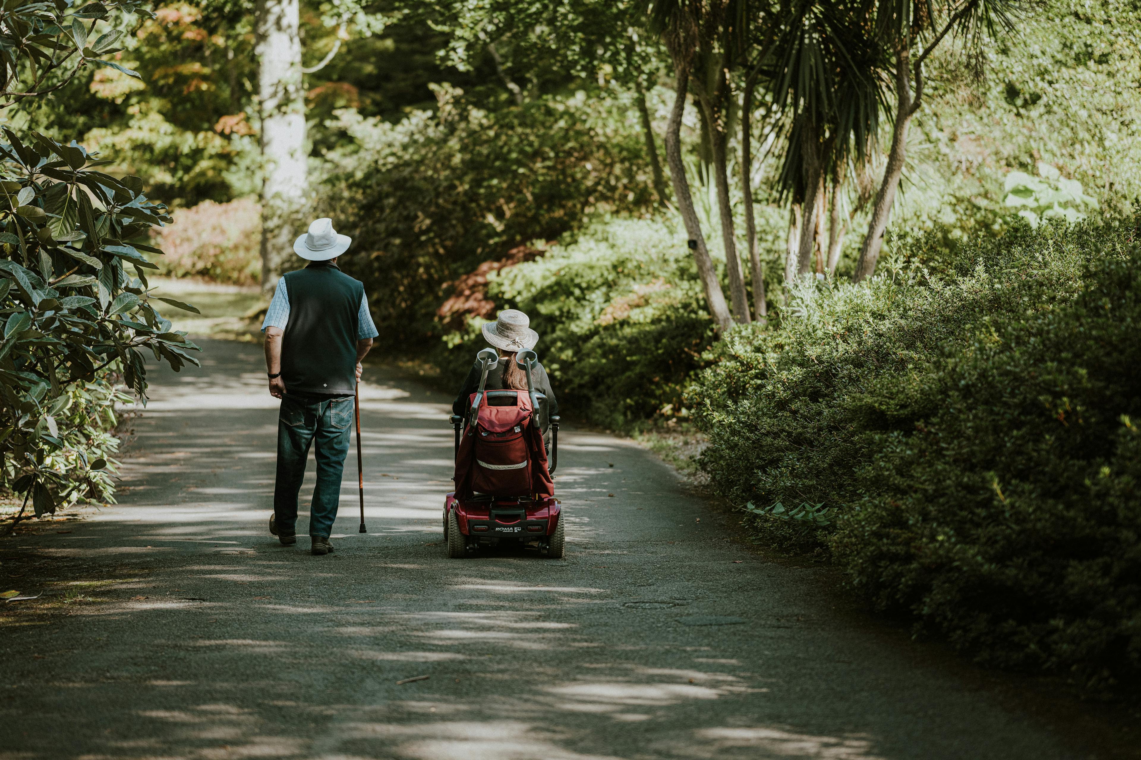 Two people walking on a path, one with a cane and one in a wheelchair.